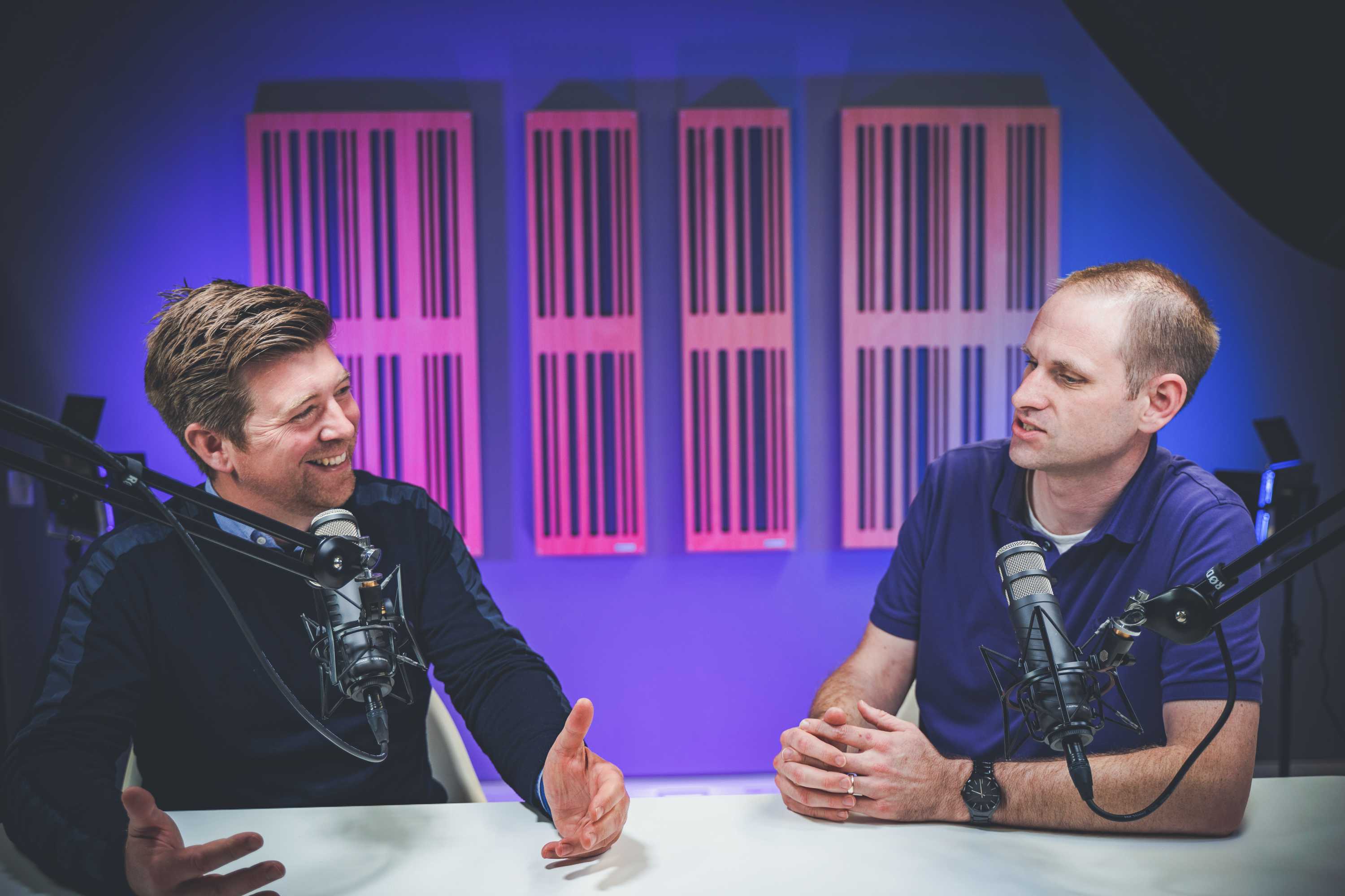 Two podcast presenters gesture whilst filming a discussion, the presenter on the left is smiling.