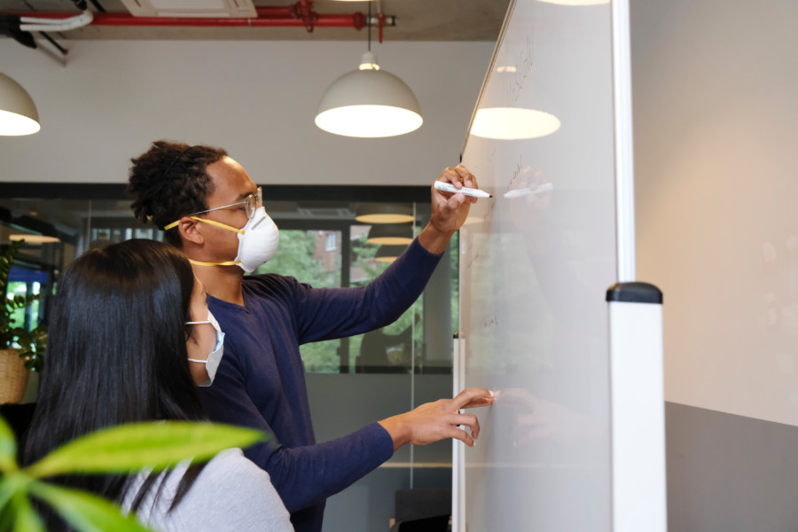 two collaborators add comments to a user experience process on a whiteboard