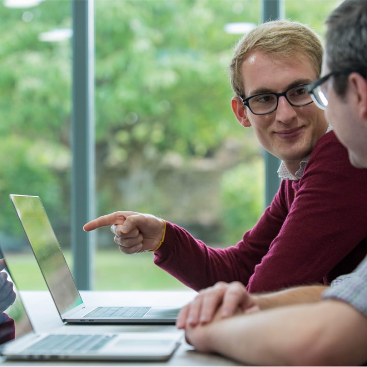 Development director points at laptop whilst discussing solutions with systems administrator.