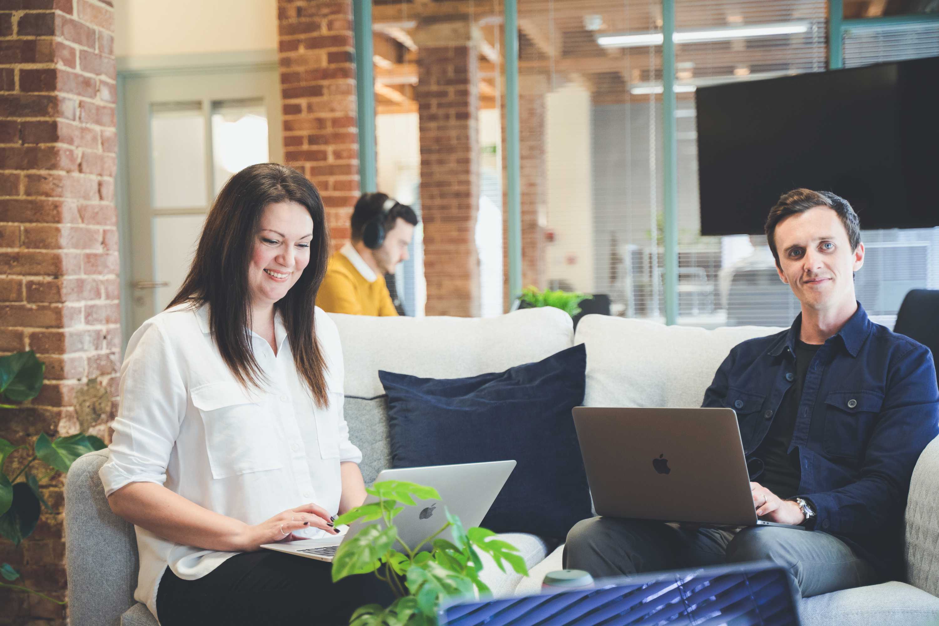 The senior project manager and creative director smile and look at their colleague out of frame. Design team chatting on sofas around a coffee table.