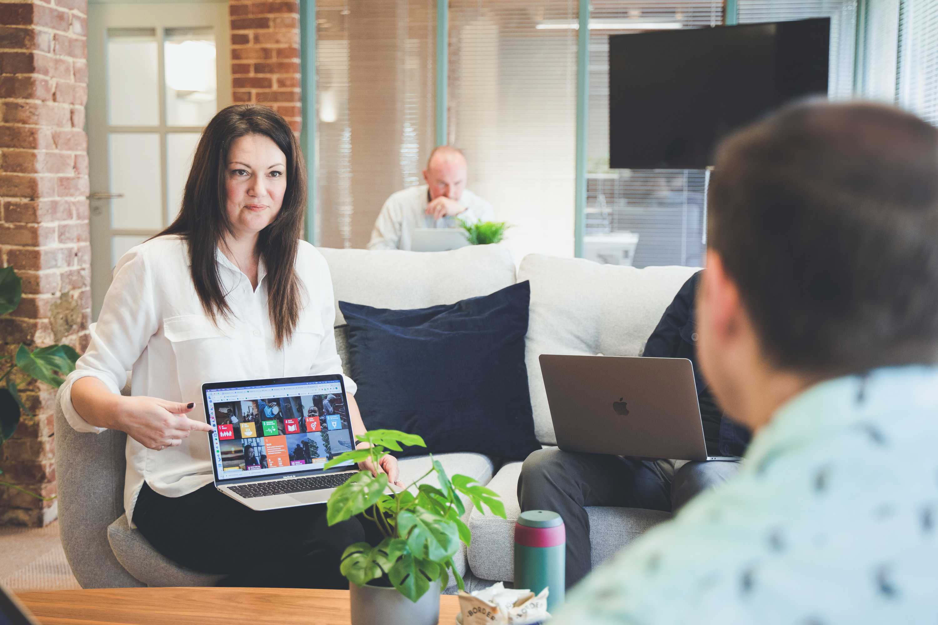 Three colleagues sat on sofas around a coffee table review and discuss an image during a design meeting.