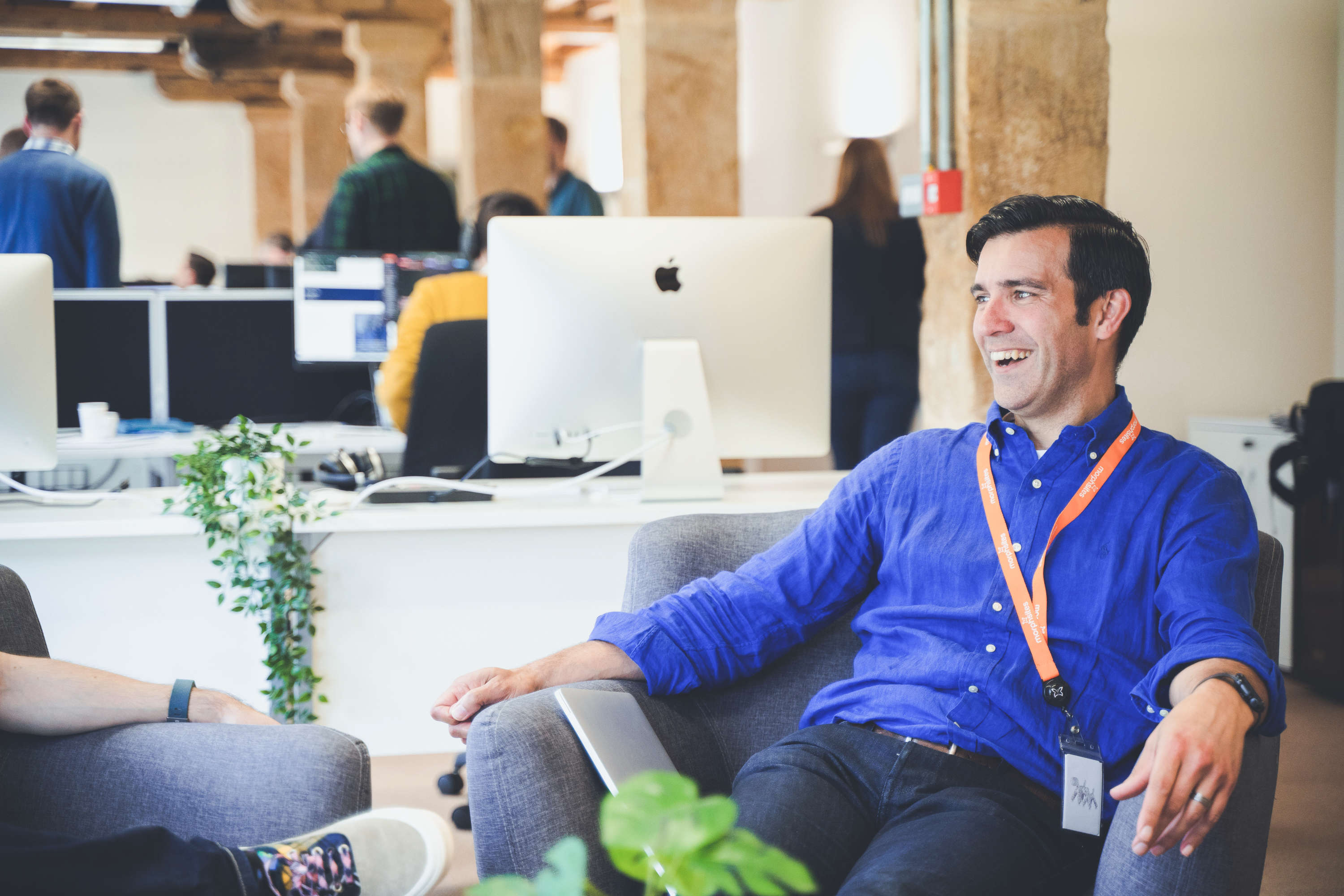 Project manager laughs whilst chatting with a colleague in a sofa chair.