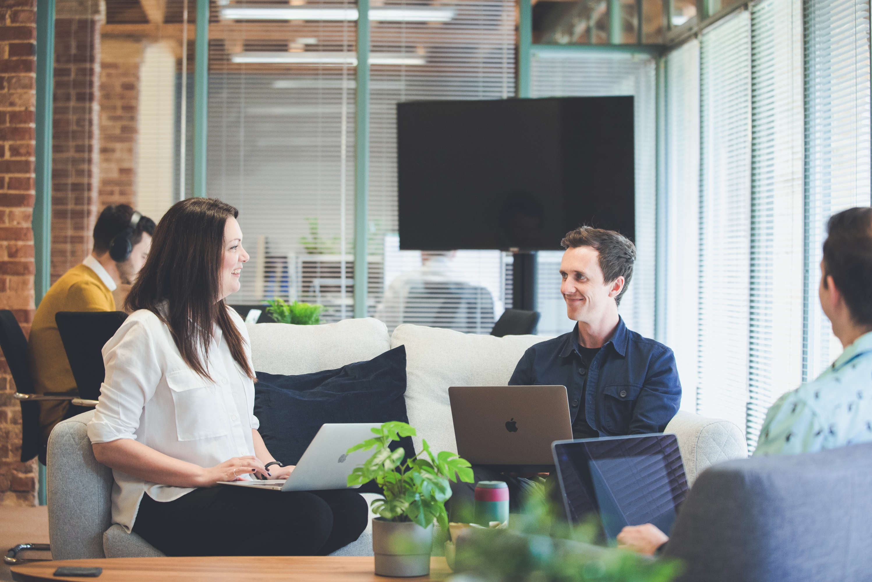 Senior designer, creative director and senior project manager sit on sofas around a coffee table and have a friendly discussion, all are smiling.