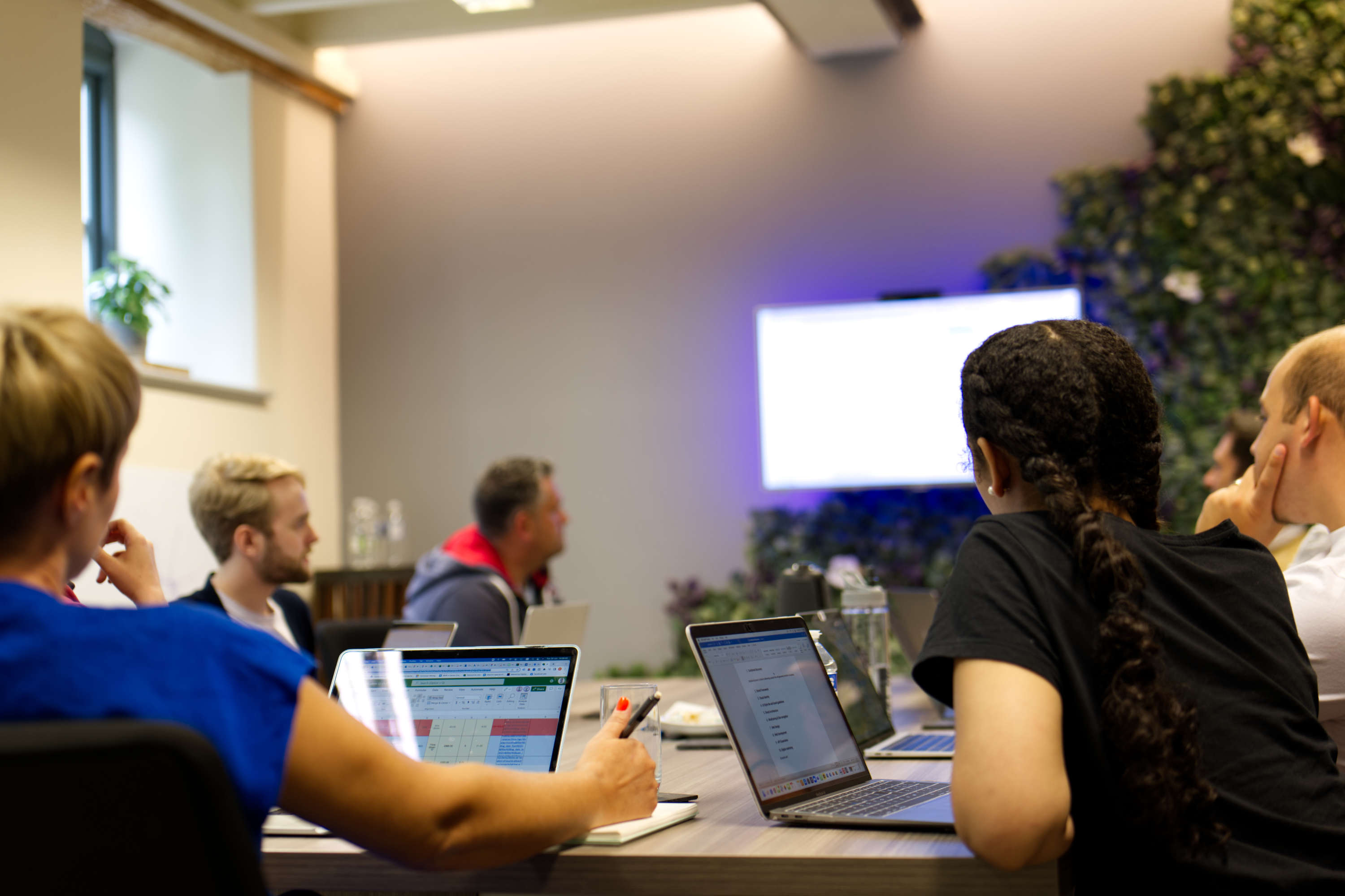 Digital marketers discuss the performance of their work around a large desk during a meeting.