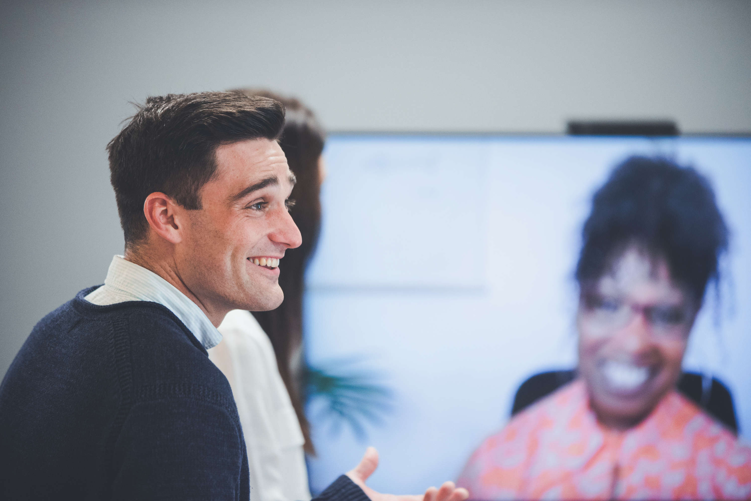 Senior client manager smiles and talks with a colleague out of frame during a group video call with other team members.