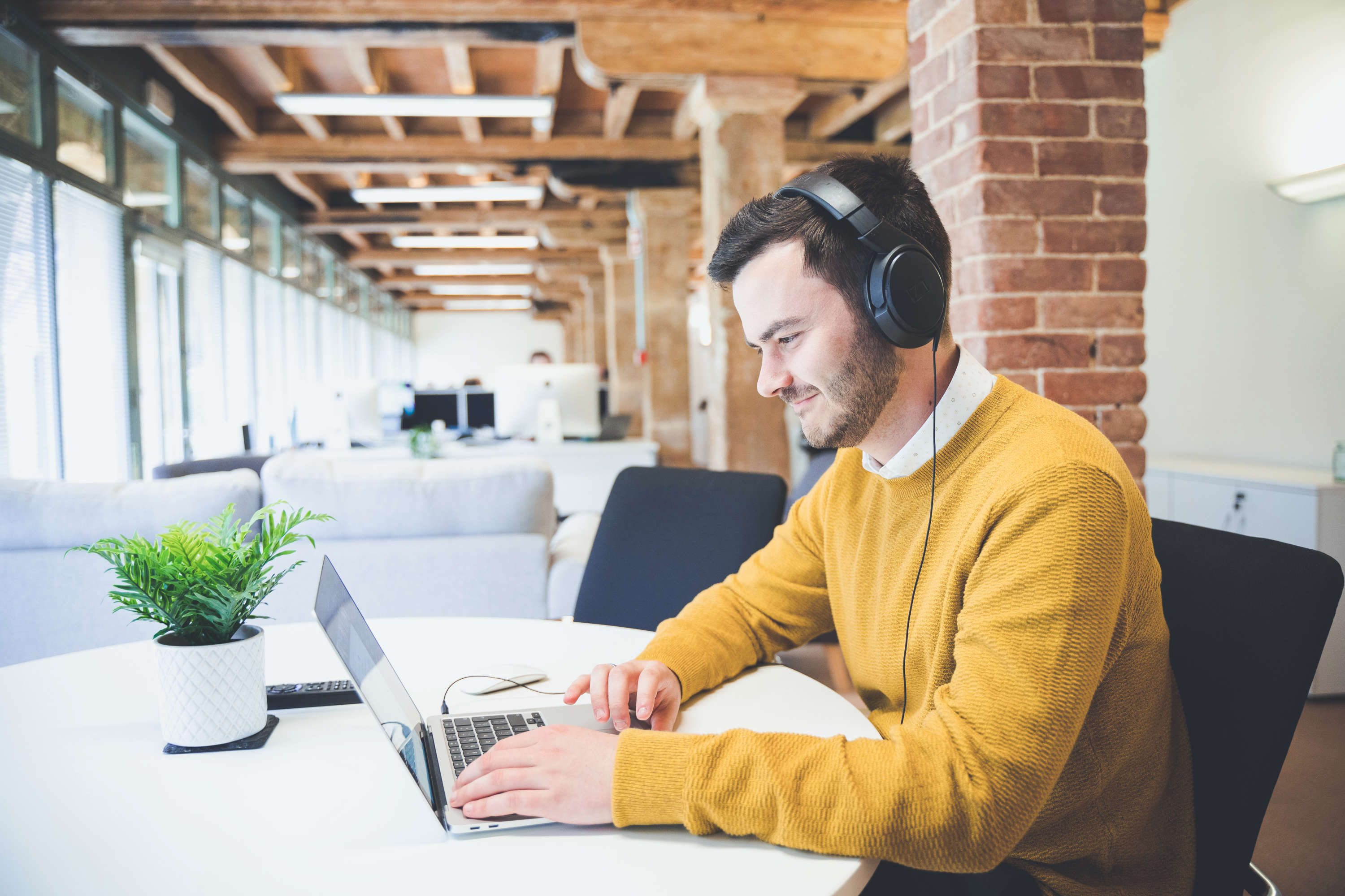 A project manager discusses a project with a client on their laptop in a bright modern office space.