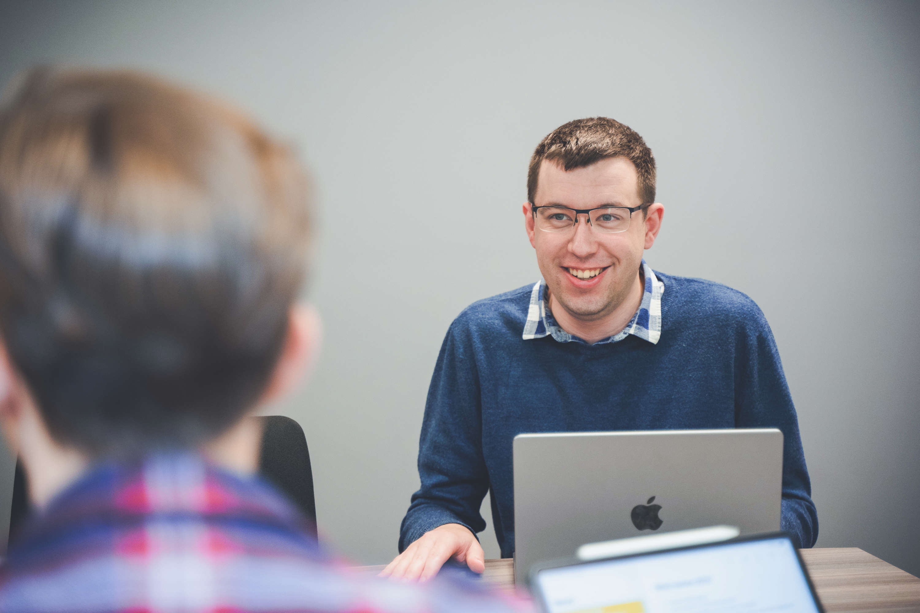 Two developers talk at a large desk with laptops, both smiling.