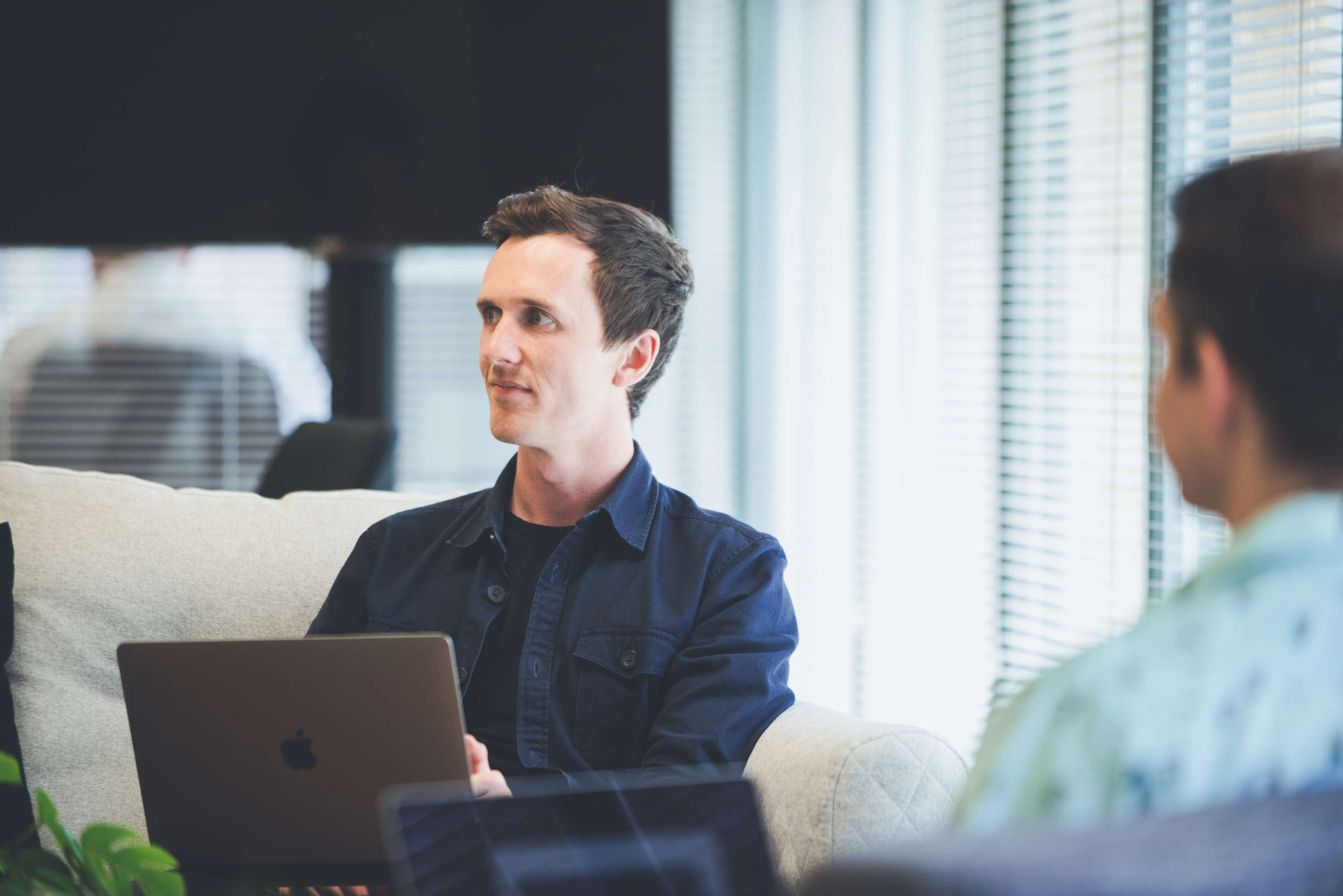 Creative director and senior designer using laptops during a discussion with colleague. Both are looking at their colleague out of frame.