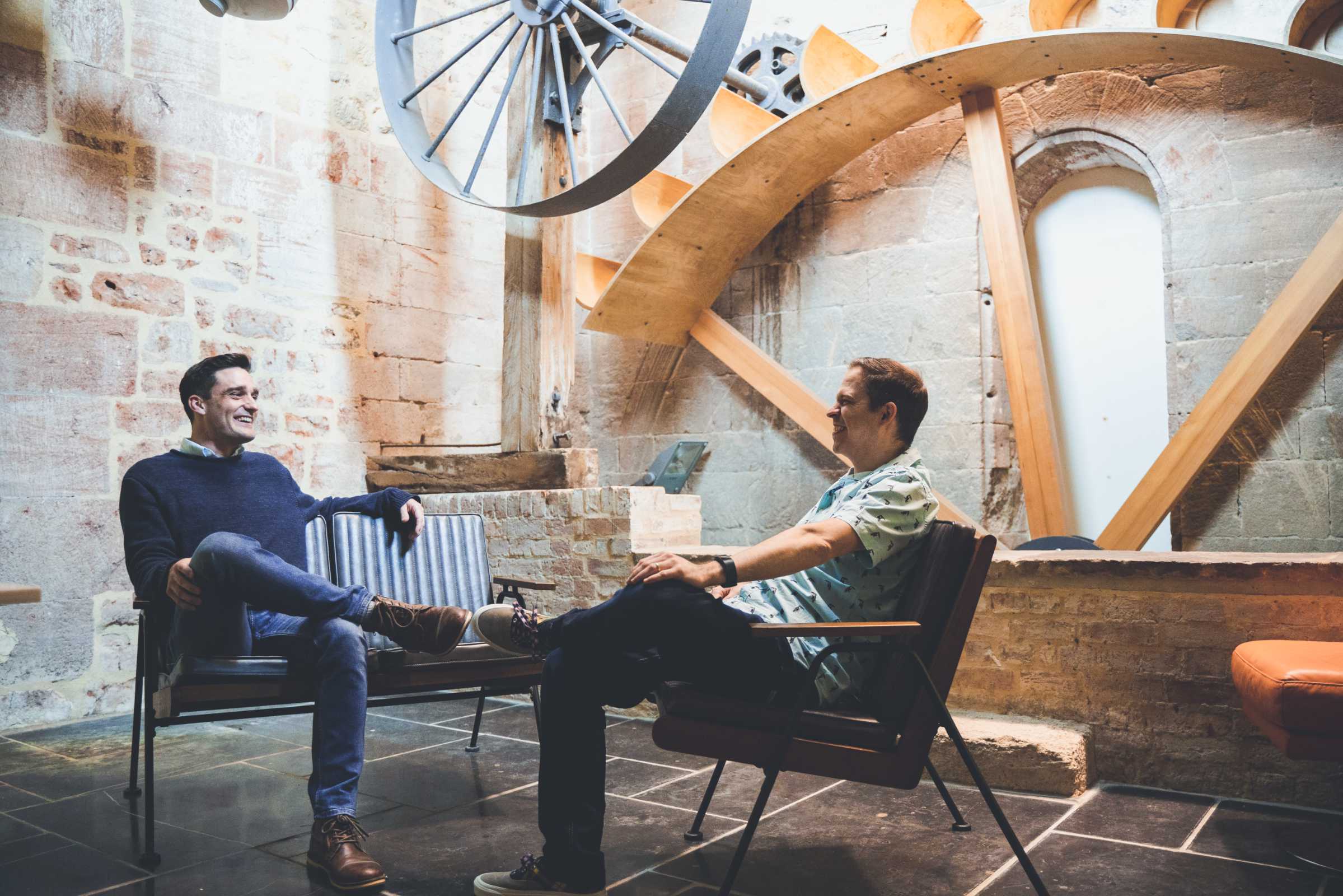Two colleagues have a chat in front of restored waterwheel in office.
