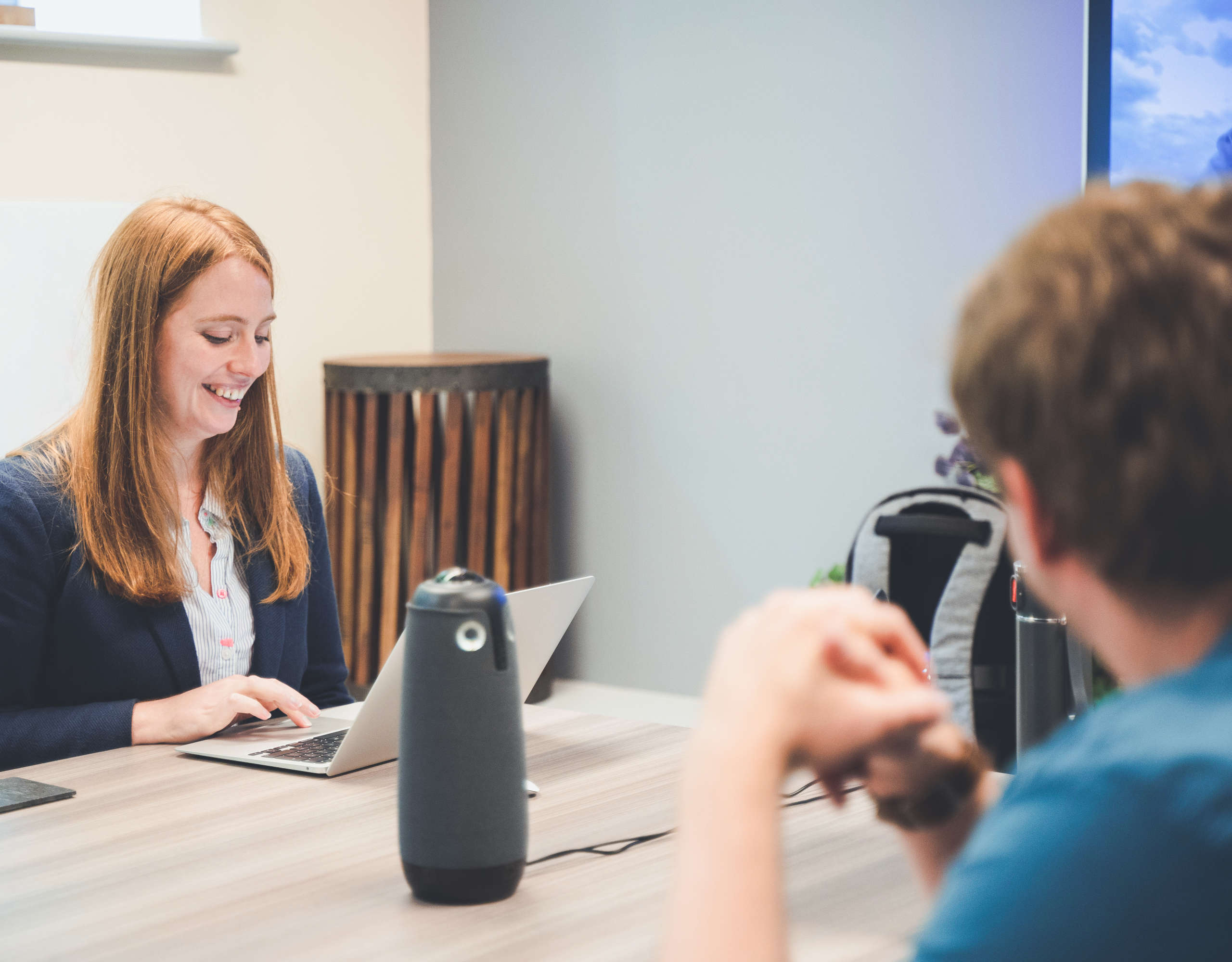 A project manager and developer sat at a large table chat before a meeting, both are smiling.