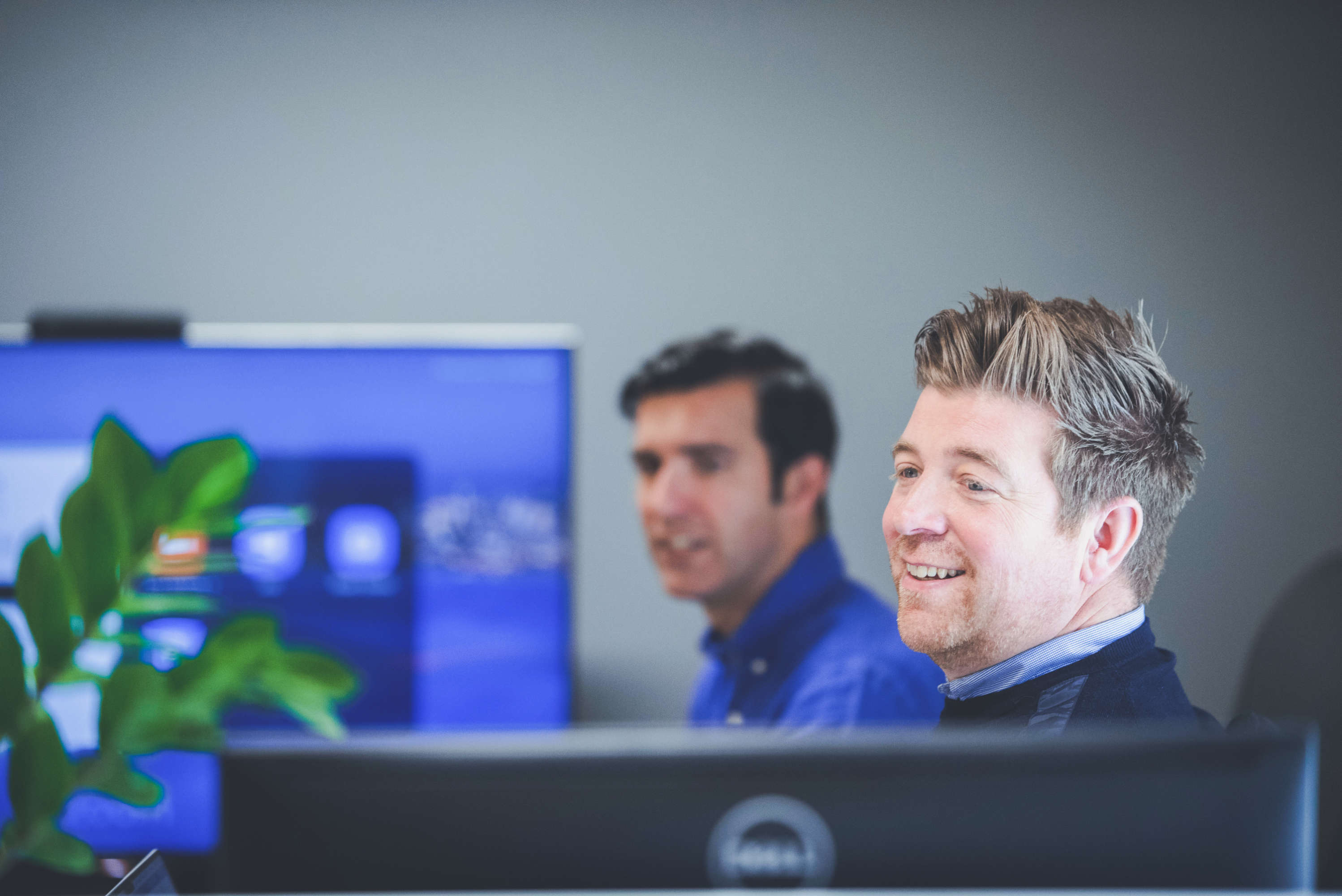 Managing director smiling whilst looking at a colleague over his monitor.