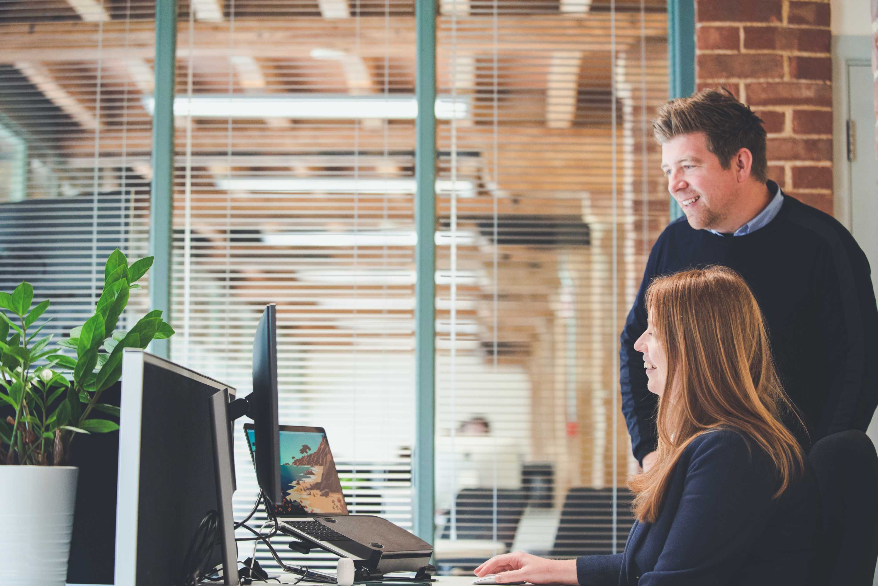 The managing director catches up with the studio manager at a desk, both are smiling and looking at a screen.