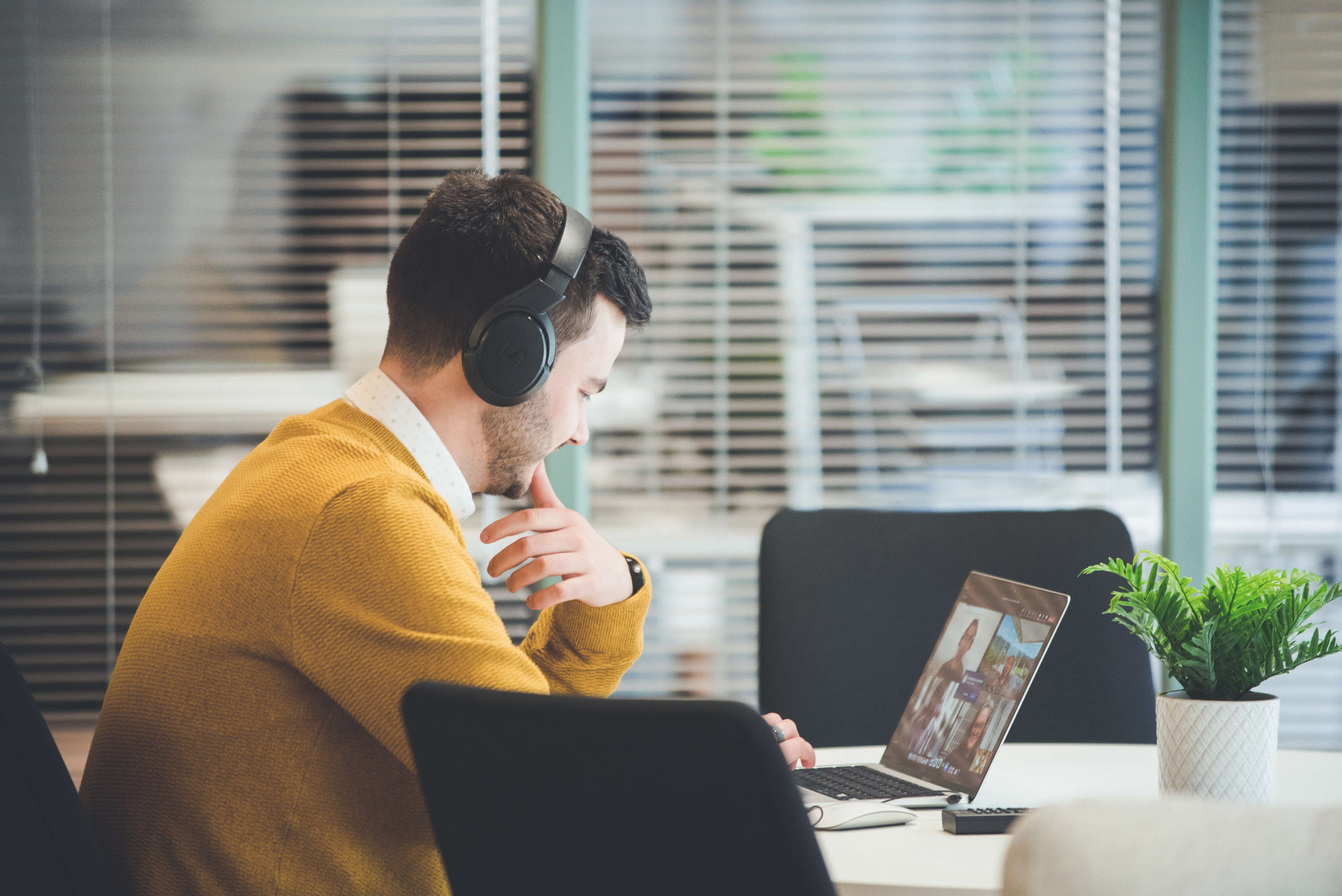 A project manager sat in front of a glass partition screen in a modern office space looks at his laptop during a video call.