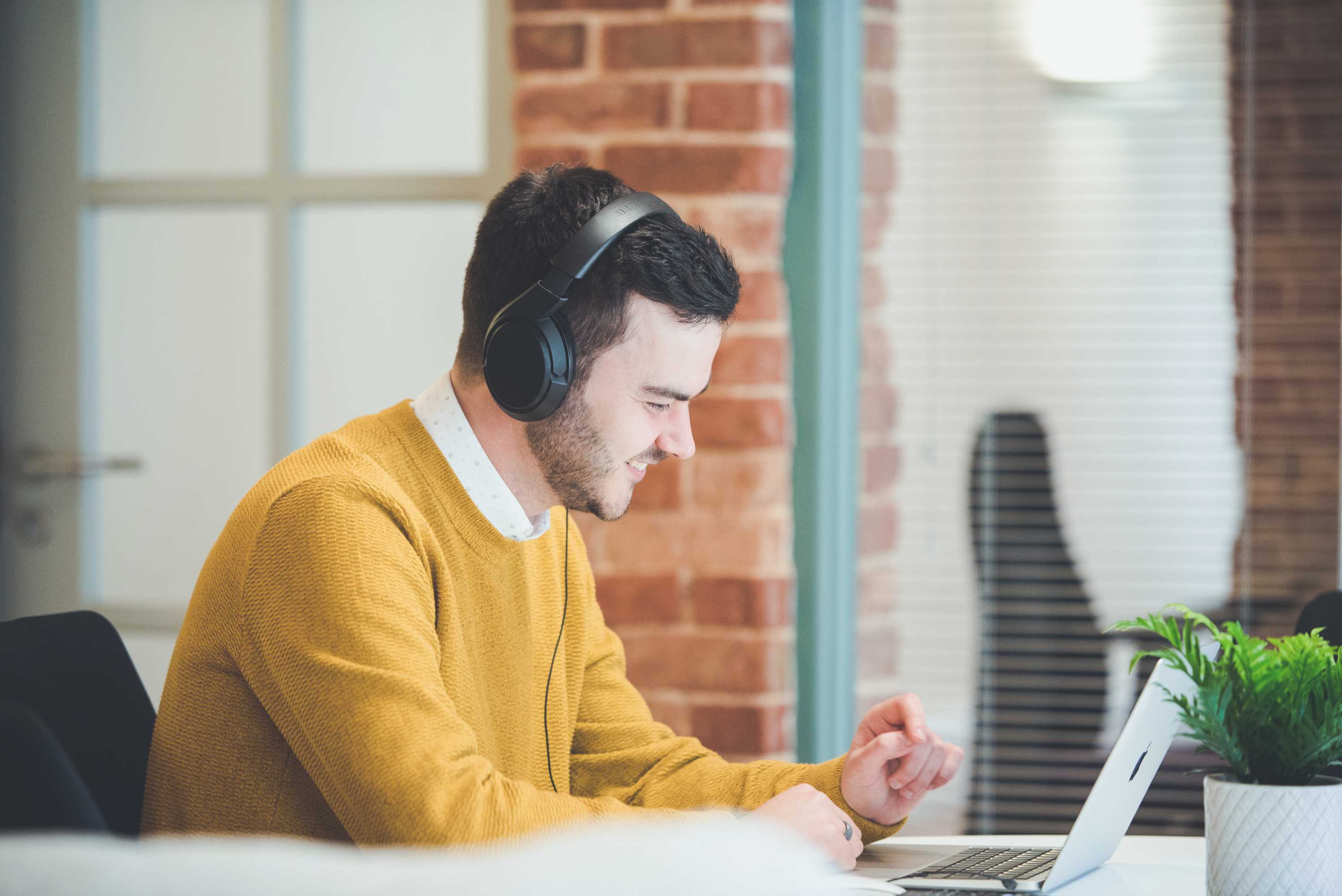 Project manager on a video call with a client, smiling and gesturing. Sitting in front of glass wall.