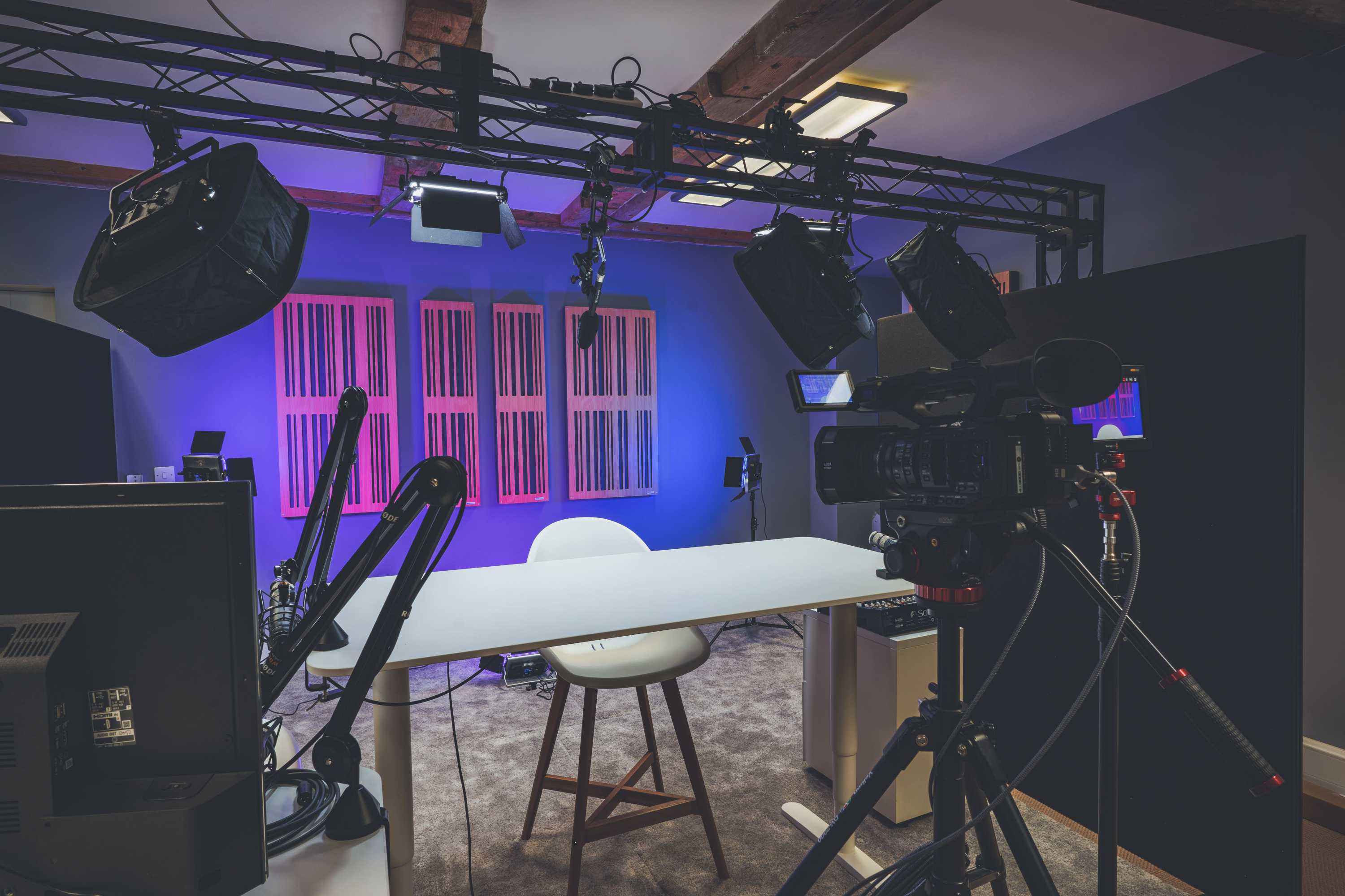 A fully equipped video studio with camera, lighting and sound equipment. The back wall is light in purple and has sound deadening panels.