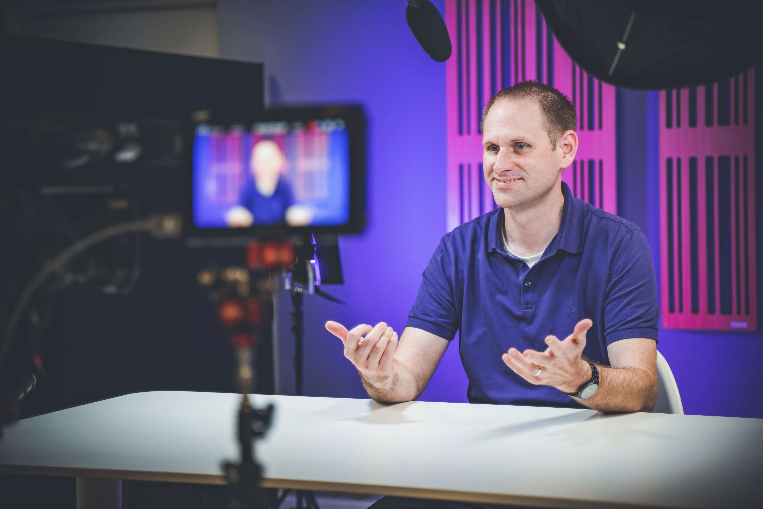 A smiling video presenter gestures to camera.