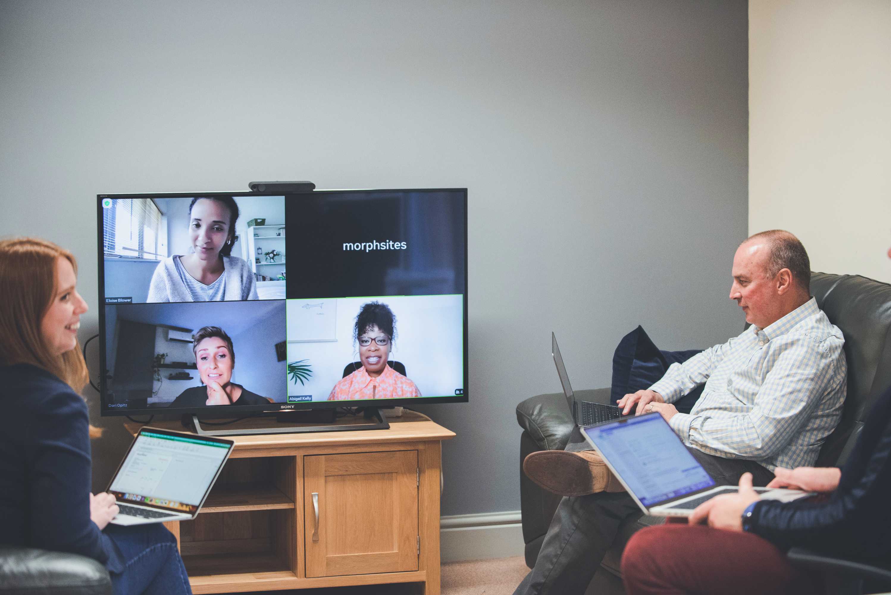 The senior management team conduct a video call with three colleagues on a large monitor.