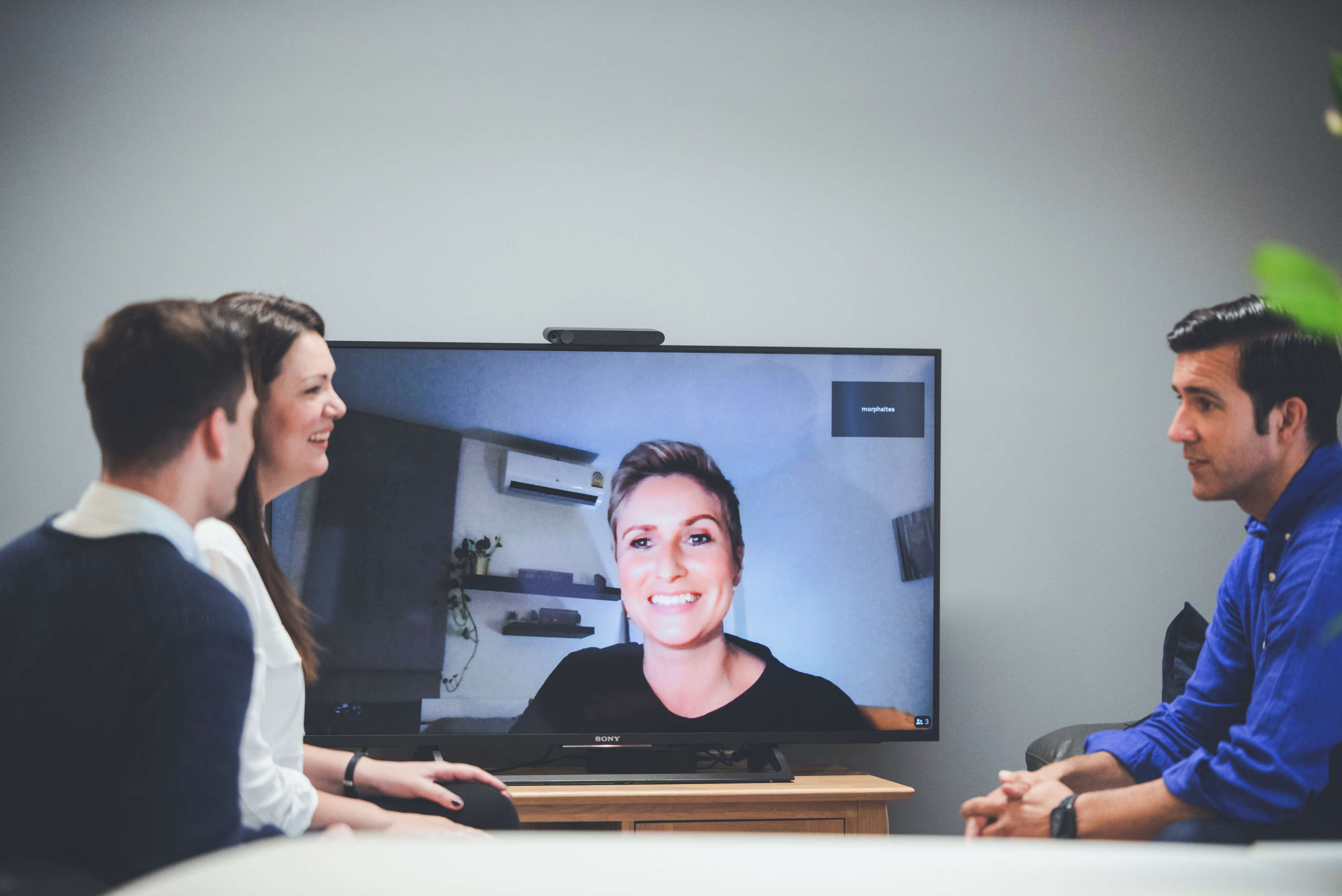 Three team members catchup with a colleague working remotely via video call.