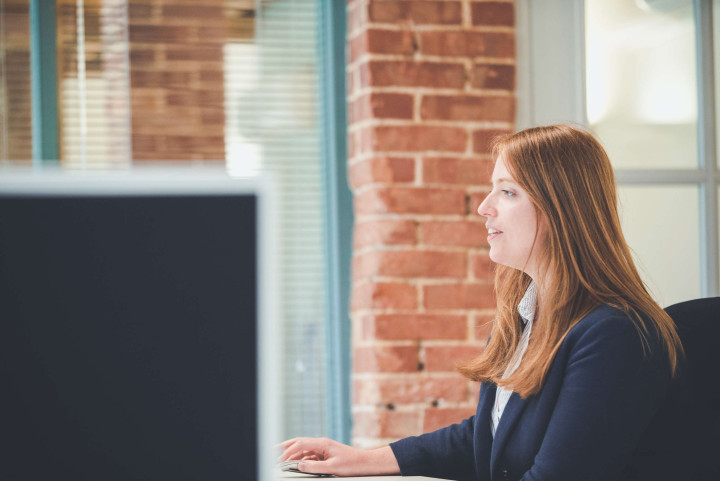 The studio manager reviewing schedules on their screen in a bright office space, with a feature brick column behind.