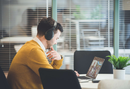 A project manager sat in front of a glass partition screen in a modern office space looks at his laptop during a video call.