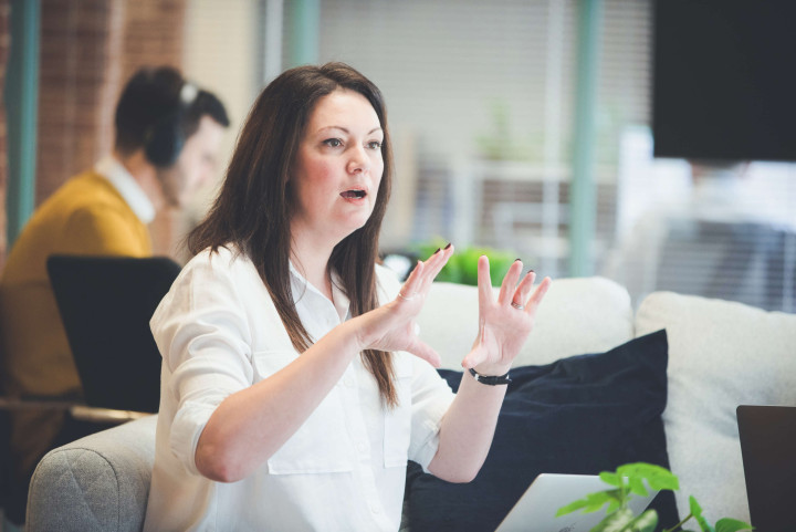 A project manager accentuates their point with hand gestures whilst talking with a colleague who is out of frame.