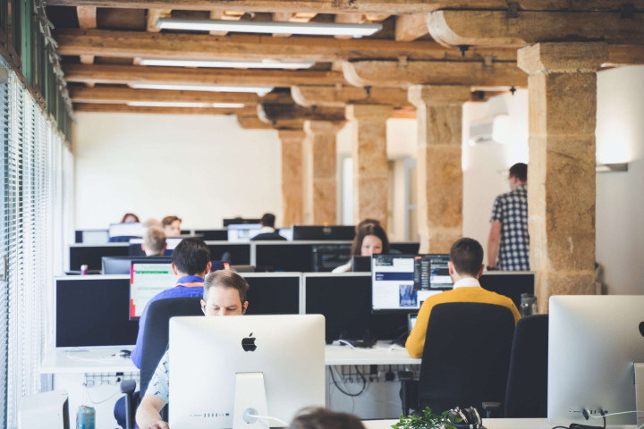 Team members working at desks in a modern rustic office space with stone pillars and glass windows.