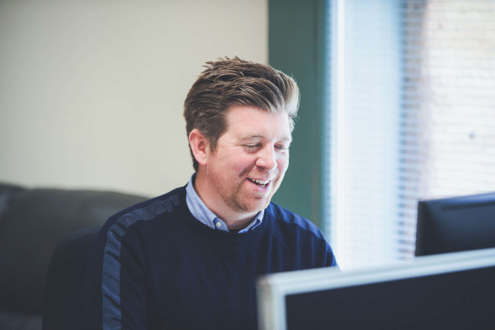 Managing director smiling whilst reviewing emails on monitor.